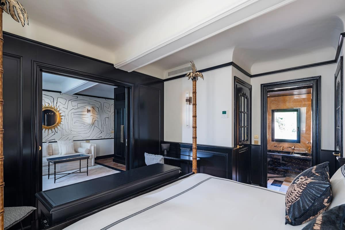 Une chambre d’hôtel moderne dotée d’un grand lit, d’un coin salon avec une table et des chaises, d’un mur décoratif et d’un grand miroir.