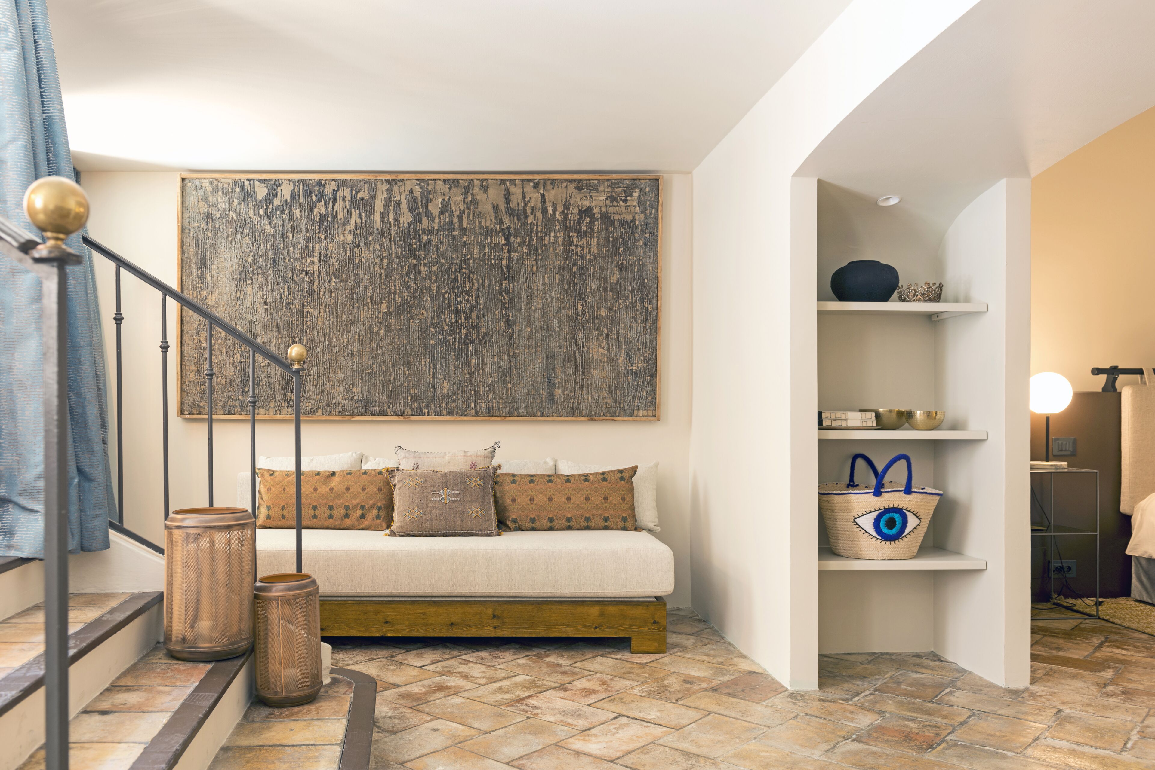 Une pièce chaleureuse avec un canapé, un grand tableau abstrait et une étagère ornée d’objets décoratifs.