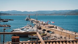 Un puerto deportivo con barcos amarrados, un muelle con gente y montañas al fondo.