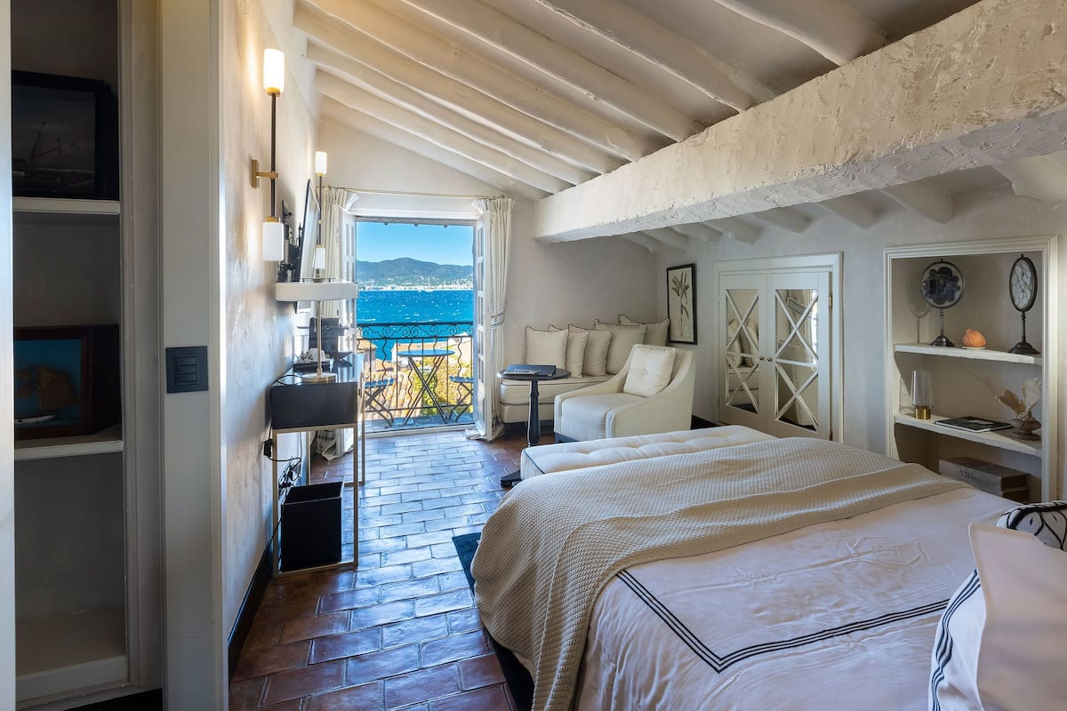 Une chambre avec un grand lit, une chaise, une petite table et une vue sur la mer.