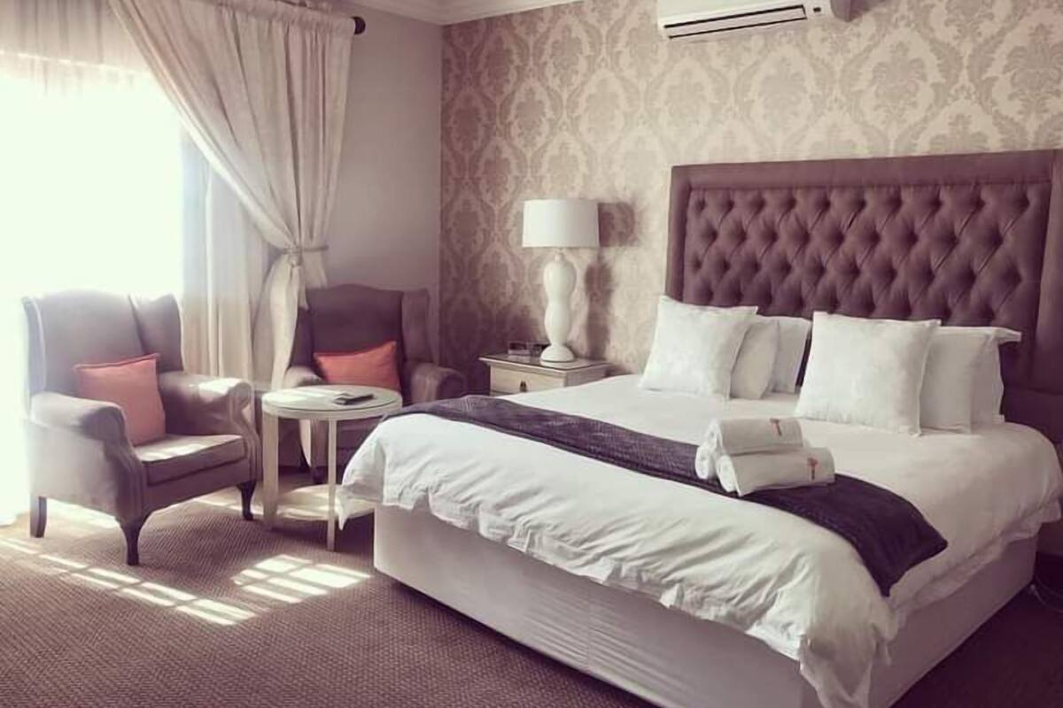 A hotel room with a large bed, a chair, a small table, and an air conditioning unit.