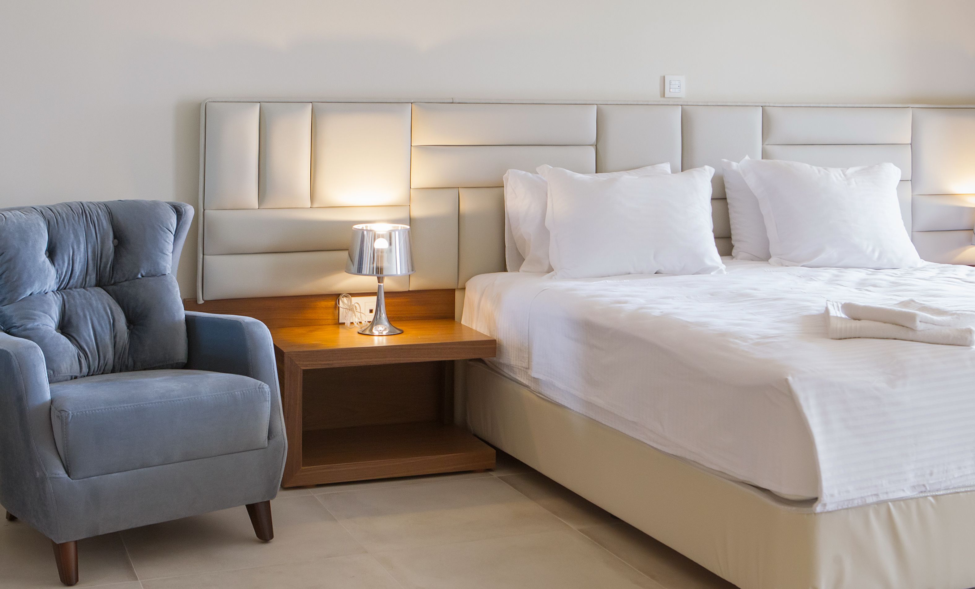 Een keurig opgemaakt slaapkamer met een bed, een nachtkastje, een lamp en een stoel.