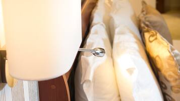 A hotel room with a bed, pillows, a bedside table with a bottle of champagne, strawberries, and glasses.