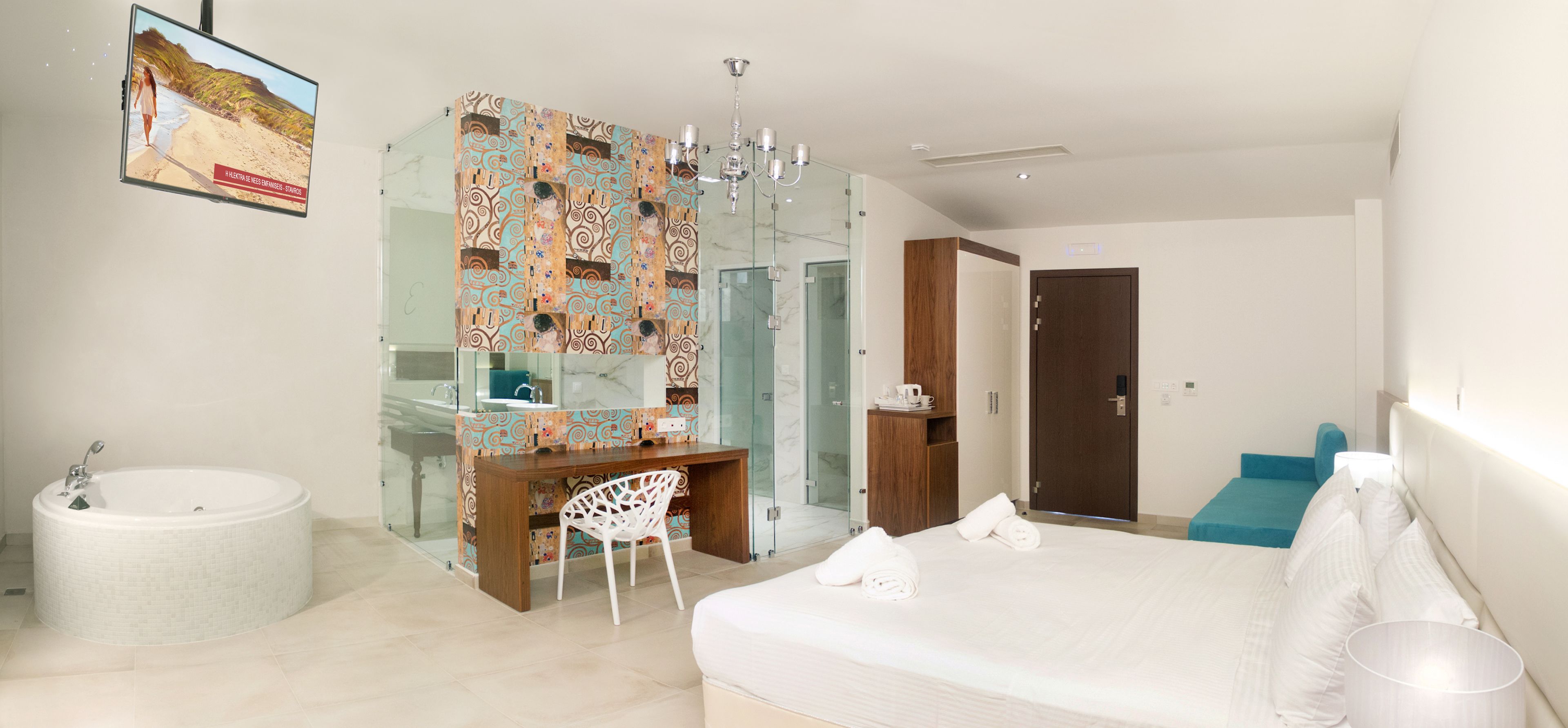 A modern hotel room with a large bed, a round bathtub, a desk with a chair, a glass shower enclosure, and a television mounted on the wall.