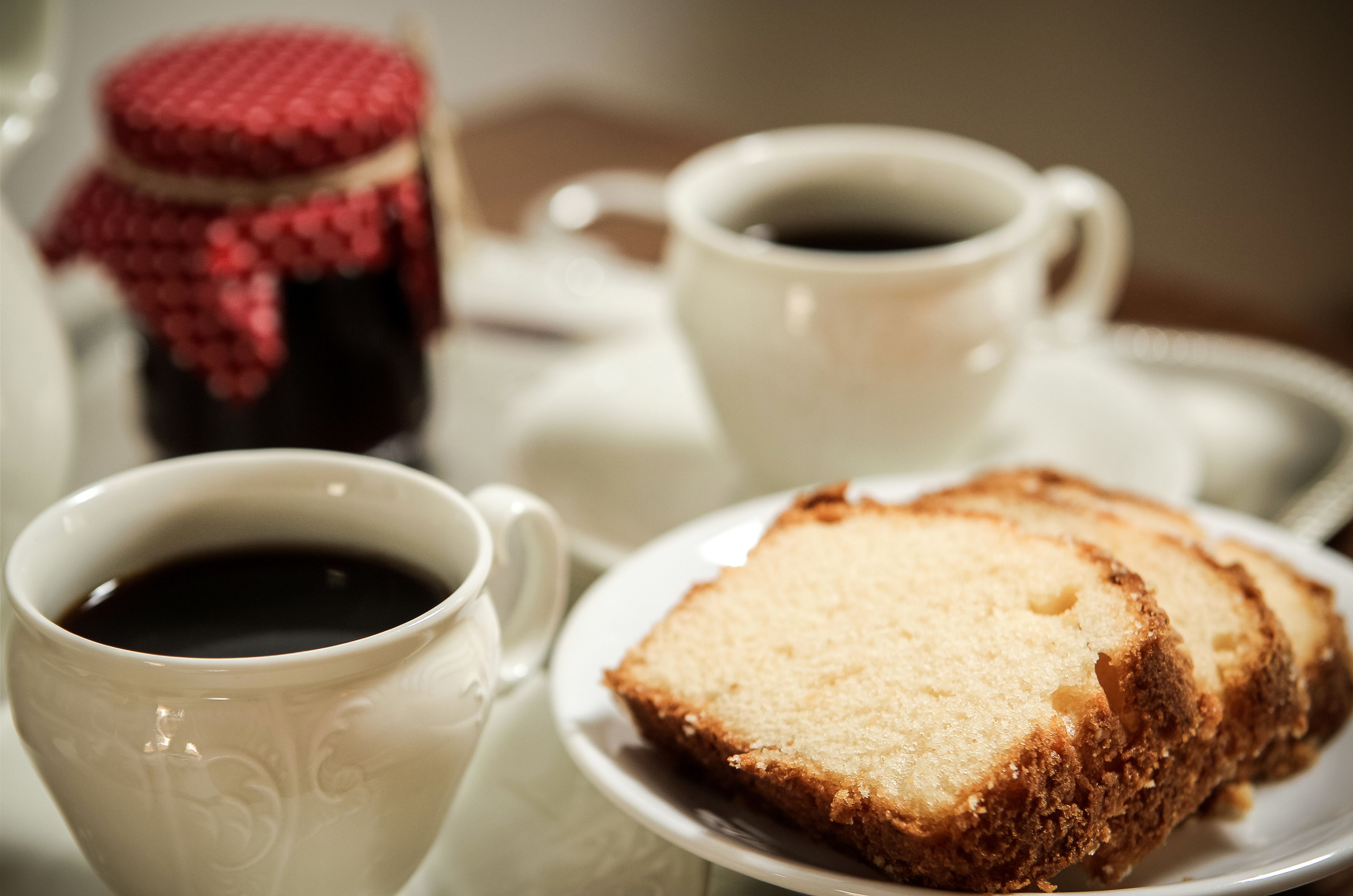 Une vue rapprochée d’une tasse blanche contenant du café, d’une part de gâteau sur une assiette et d’un pot de confiture.