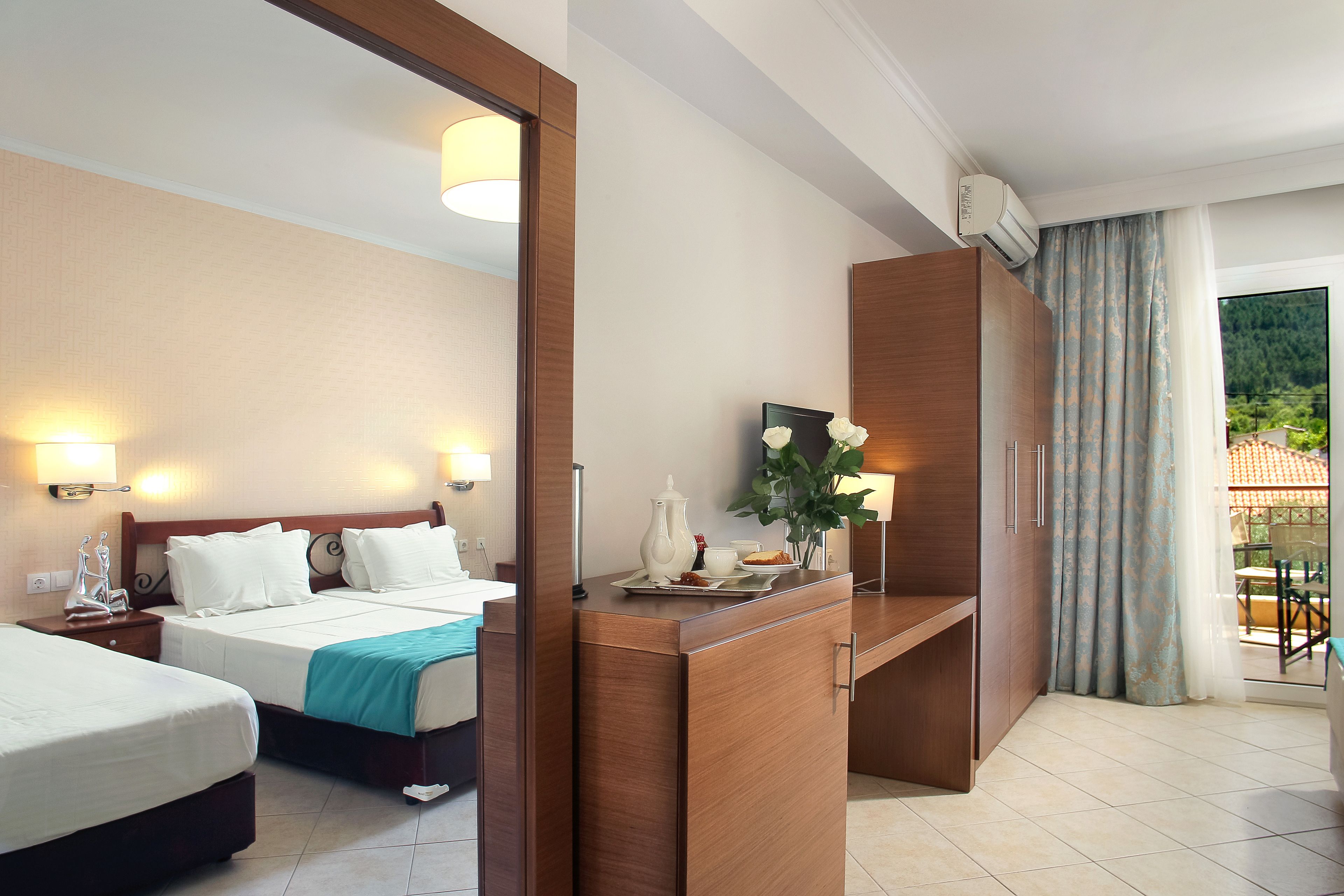A hotel room with two beds, a wooden desk, a mirror, and a view of the outdoors.