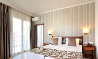 Una habitación de hotel con una cama grande, dos mesitas de noche, un ventanal con cortinas y aire acondicionado instalado en la pared.