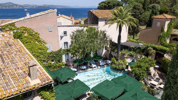 Piscina en la azotea con sombrillas verdes, vista despejada al mar y edificios circundantes.