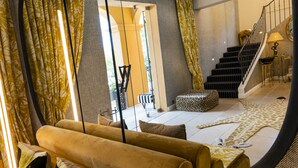 A living room with a sofa, patterned curtains, a staircase, and a leopard print ottoman. - Hôtel Le Y Saint-Tropez (Saint-Tropez)