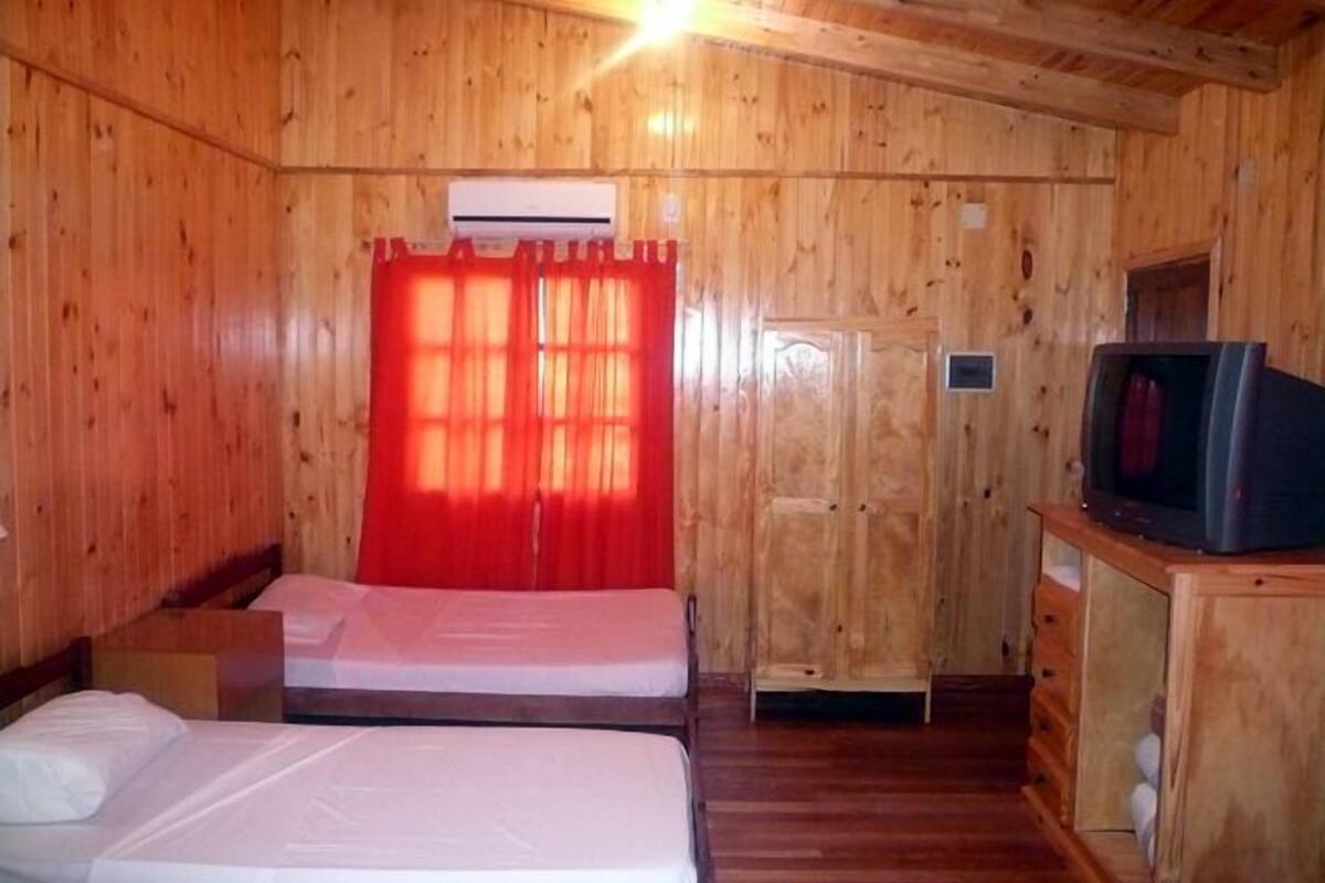 A wooden cabin room with two beds, a TV, and a small table.