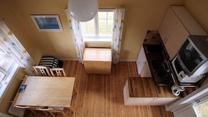 A compact kitchen with a wooden table, a small seating area, and a television. - Pensionat Lövängen (Ljugarn)