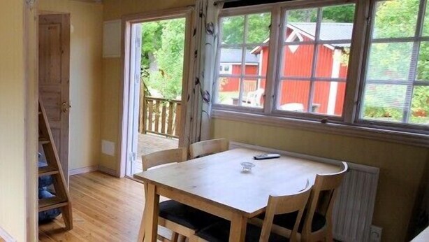 A small, cozy room with two single beds, a wooden table, and a window with a view of a red building. - Pensionat Lövängen (Ljugarn)