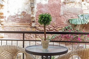 A round table with a potted plant in the center, surrounded by wicker chairs, against a textured wall with a brick pattern. - Casa Kasteli (Chania)