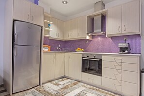 A modern kitchen with light wood cabinets, a stainless steel refrigerator, an oven, and a purple-tiled backsplash. - Casa Kasteli (Chania)