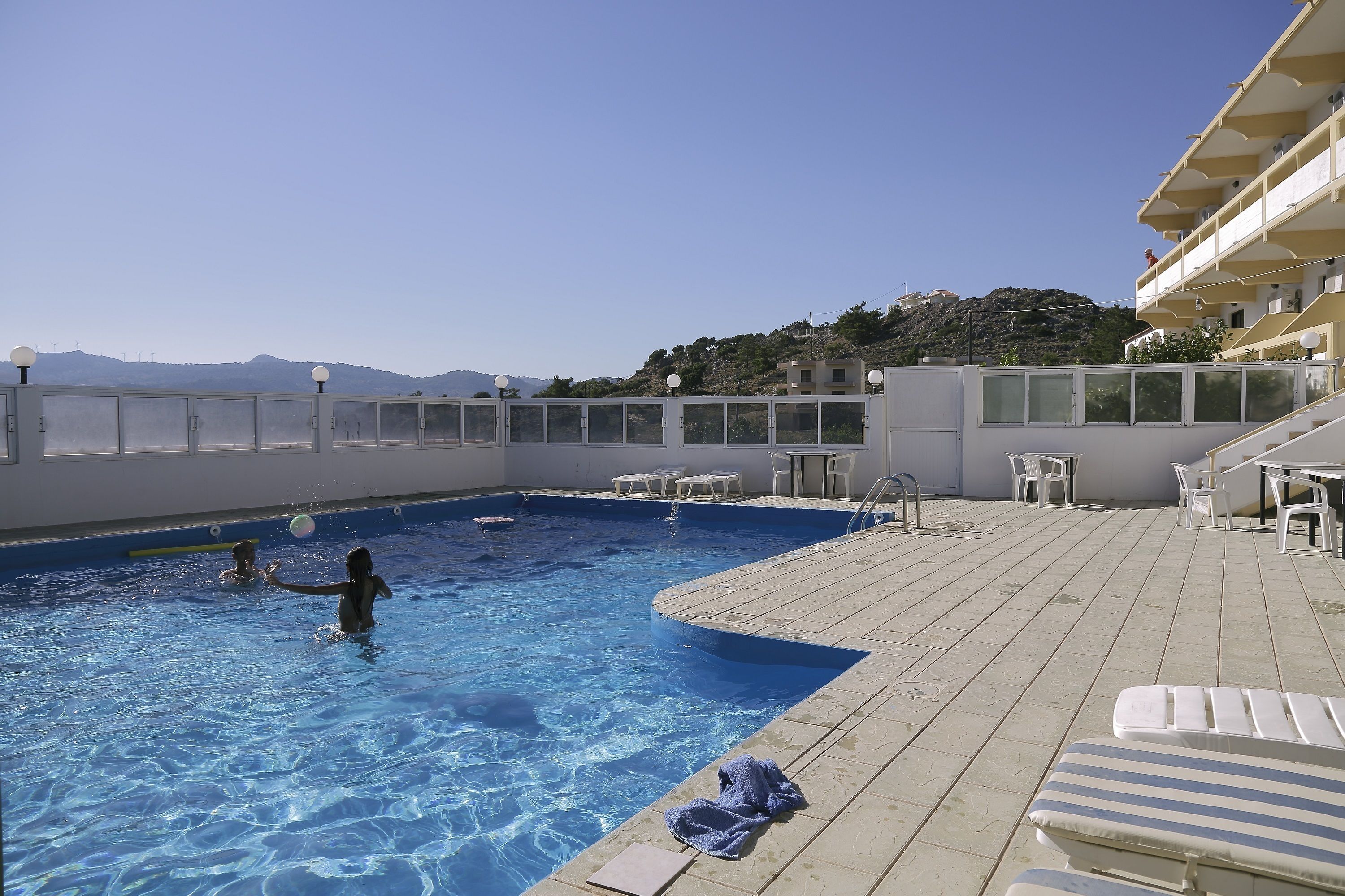 A swimming pool with clear blue water, surrounded by a deck with lounge chairs and tables.