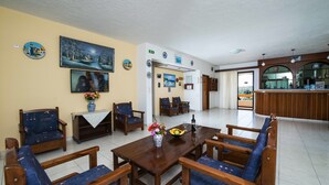 Uma sala de jantar com mesa de madeira e cadeiras estofadas em azul, um quadro na parede e vista para a varanda externa.