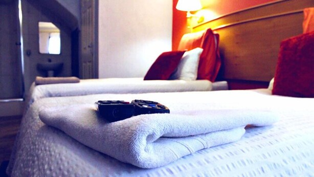 Een hotelkamer met twee bedden, elk met een witte deken en een afstandsbediening erop.