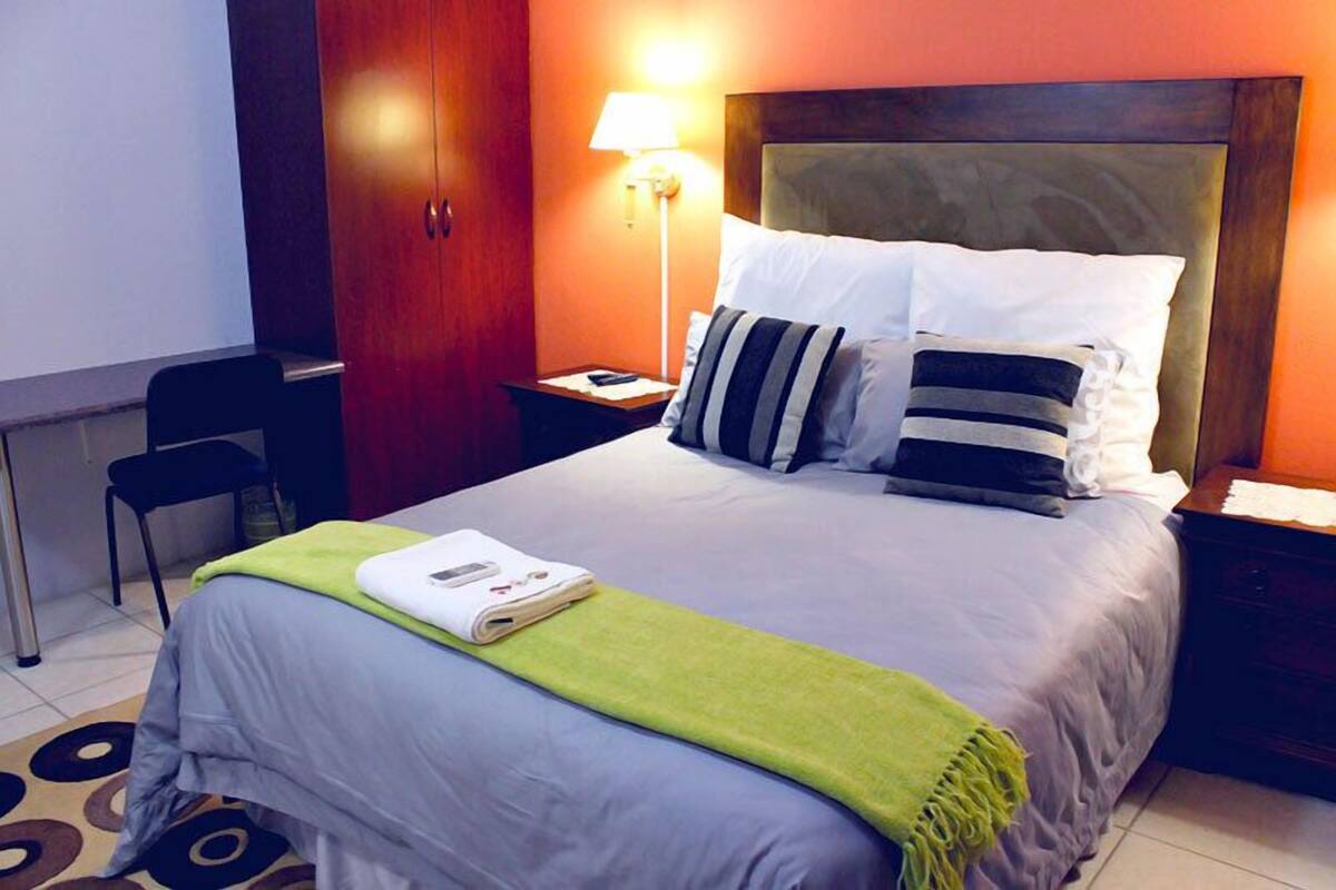 Ein Hotelzimmer mit Bett, Schreibtisch, Stuhl, Lampe und Kleiderschrank.