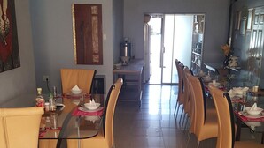 Een eetgedeelte met een glazen tafel, beige stoelen en een keuken op de achtergrond.