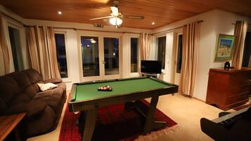 A room with a pool table, a sofa, a television, and a piano.
