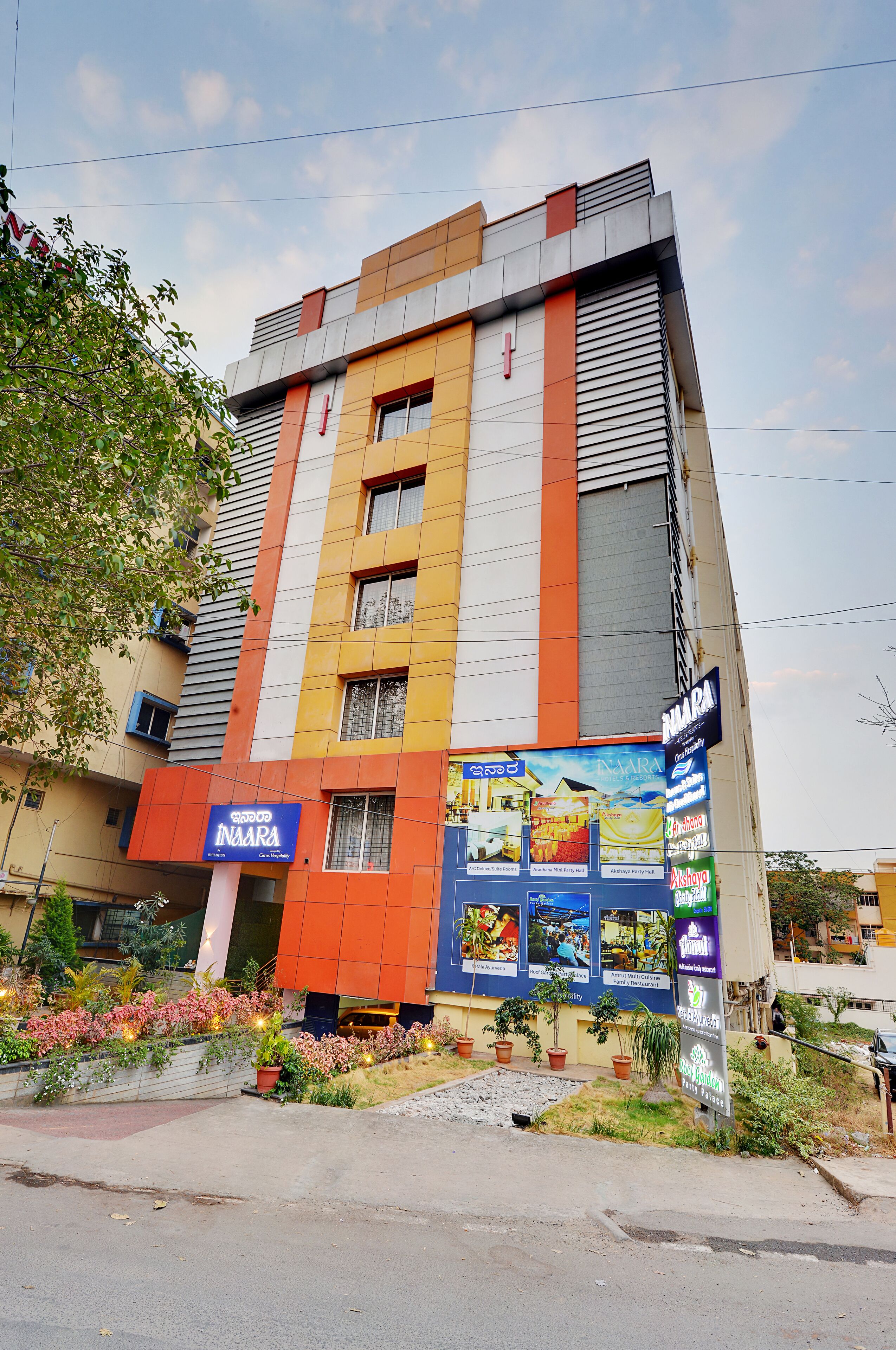 A multi-story building with a colorful facade, a signboard for 'NARA', and a small garden area with potted plants.