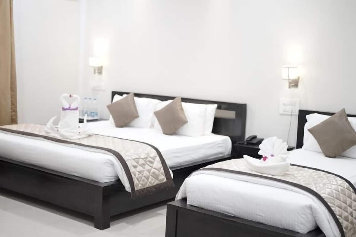 A hotel room with two beds, each with a dark headboard, white linens, and a quilted blanket. There are bedside tables with lamps and a small table with a bottle and a tissue box.