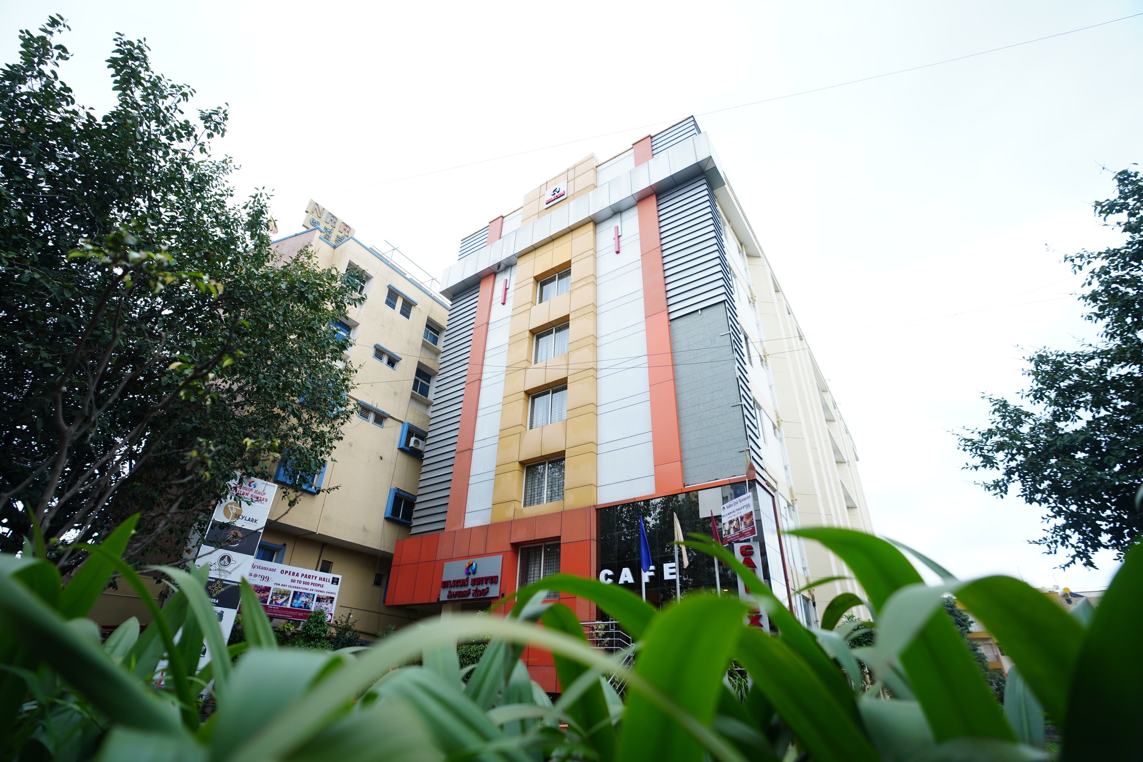 A multi-story building with a cafe on the ground floor, surrounded by greenery.