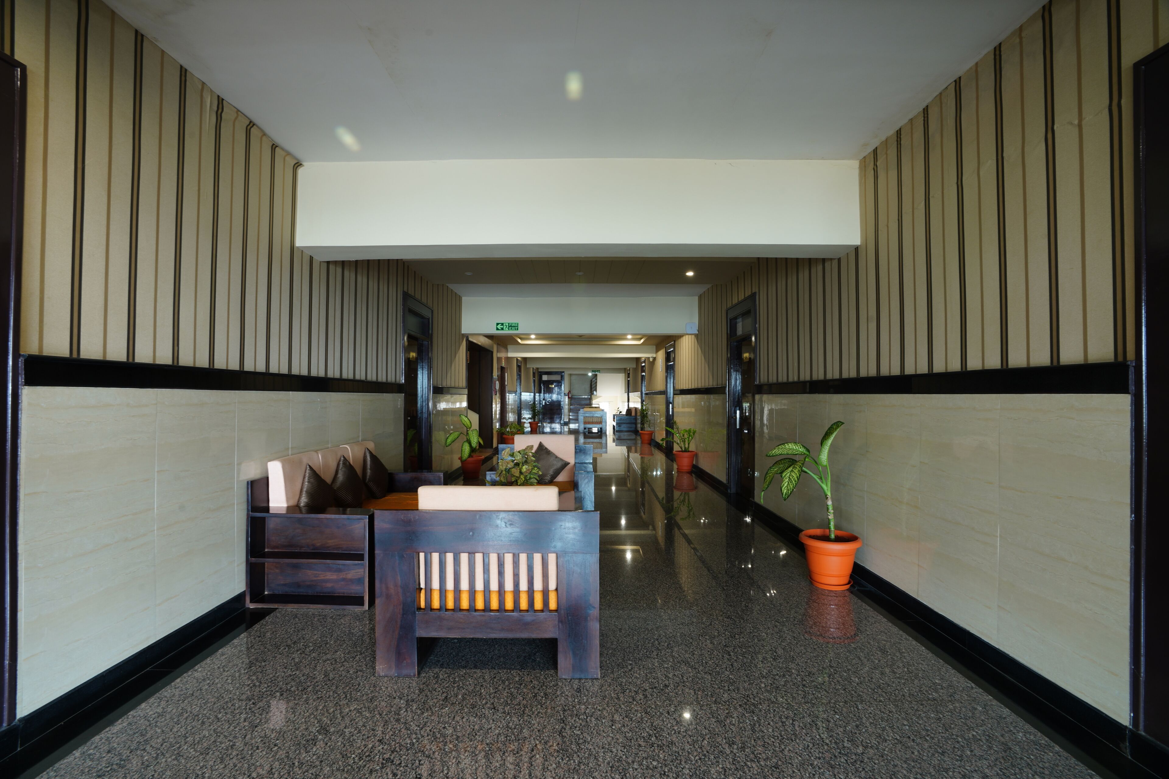 A modern hotel lobby with a central seating area, potted plants, and a polished floor.