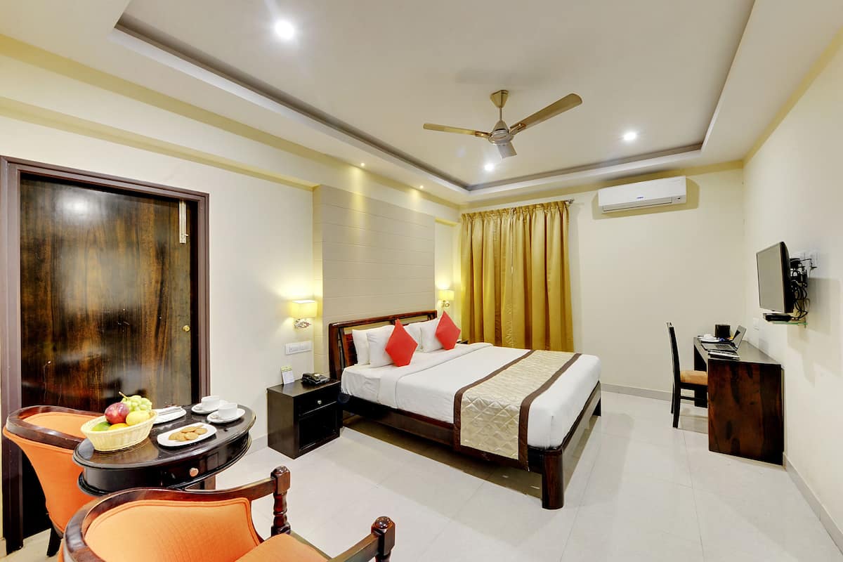 A hotel room with a bed, desk, chair, and a table with fruit and a basket.