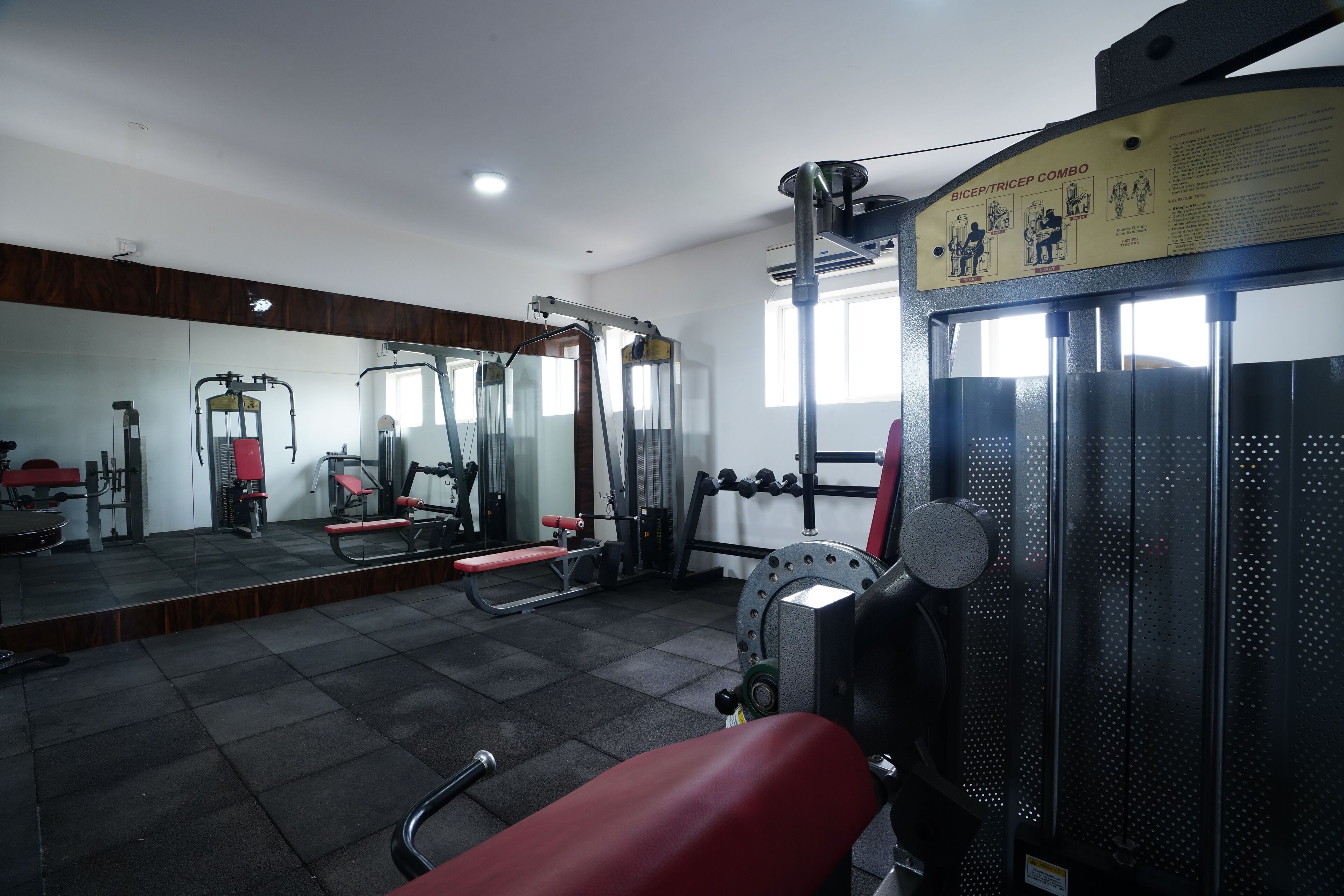 Une salle de sport équipée de divers appareils d’exercice, d’un miroir et d’un panneau indiquant les exercices à faire pour les biceps et les triceps.