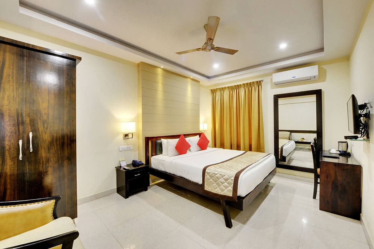 A hotel room with a bed, bedside table, nightstand, wardrobe, and a mirror.
