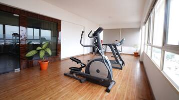 Amplia habitación con piso de madera, un ventanal grande y equipo de ejercicio que incluye una bicicleta estática y una elíptica.