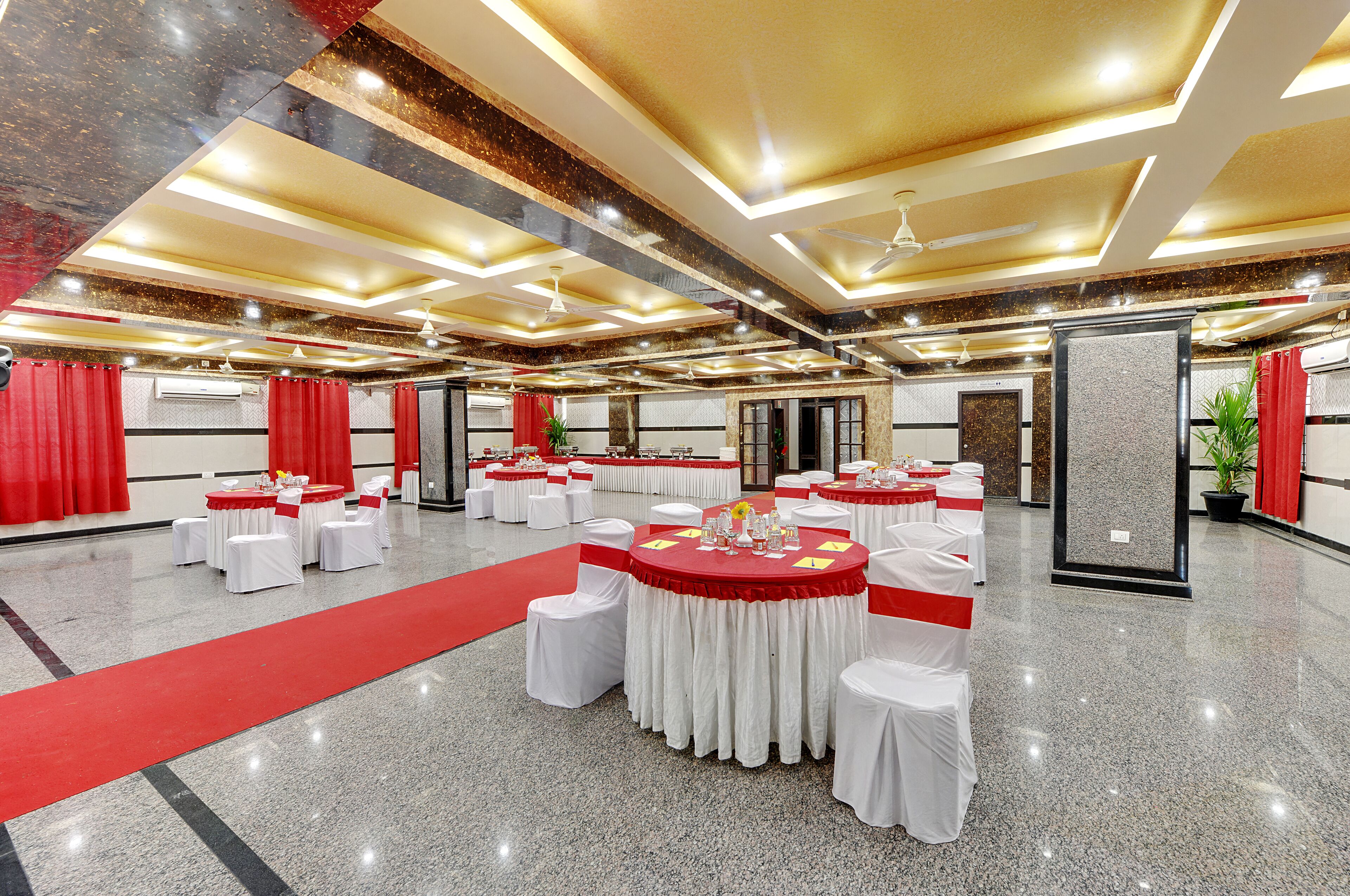 A spacious banquet hall with round tables, white chairs, and red accents.