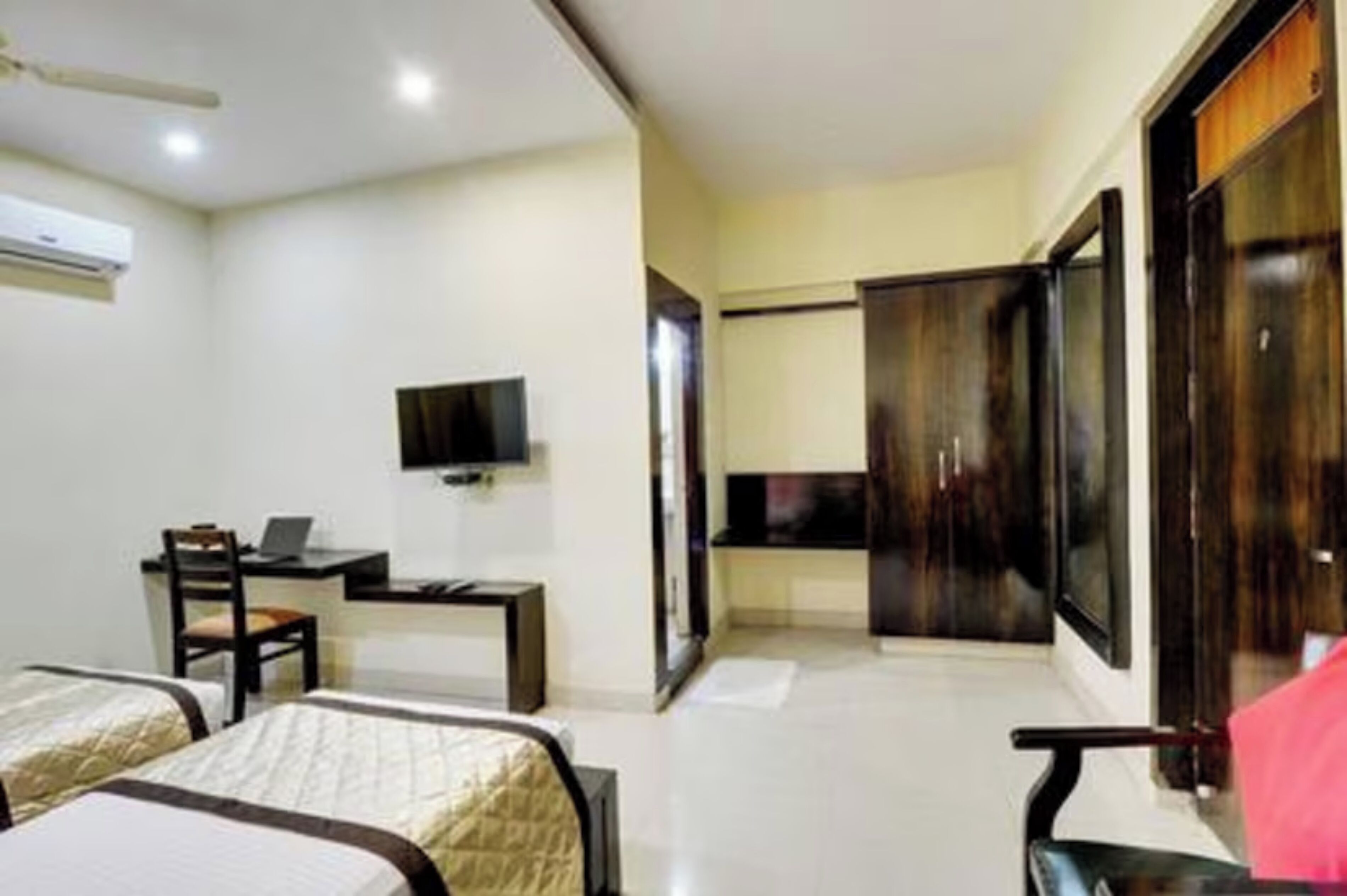A hotel room with two beds, a desk with a chair, a television, and a wardrobe.