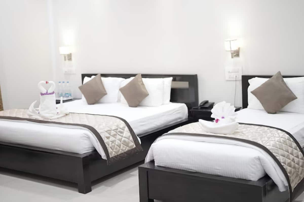 A hotel room with two beds, each with white bedding and brown headboards. There are bedside tables with lamps and a nightstand.