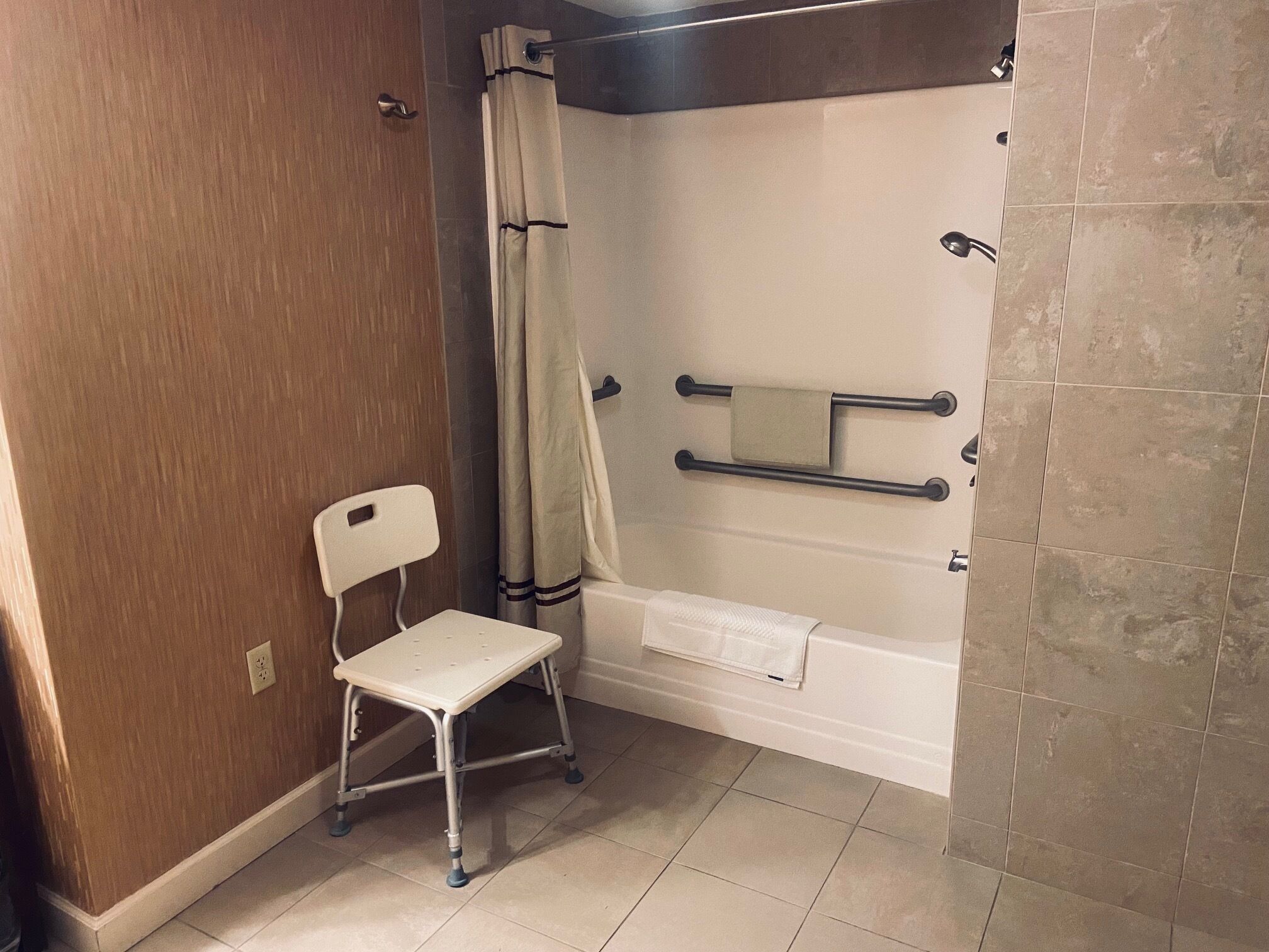 Een badkamer met een douche, een witte stoel en een handdoekhouder.