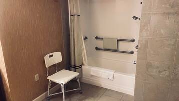 Een badkamer met een douche, een witte stoel en een handdoekhouder.