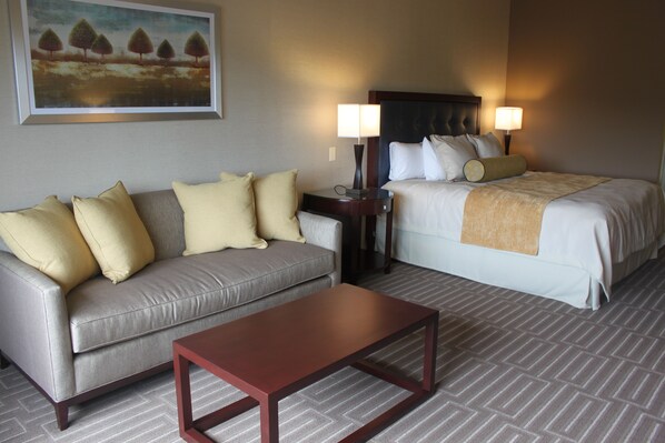 A hotel room with a sofa, a bed, a nightstand with lamps, and a painting on the wall.