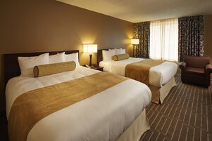 Habitación de hotel con dos camas, una silla y una mesita de noche con lámpara.