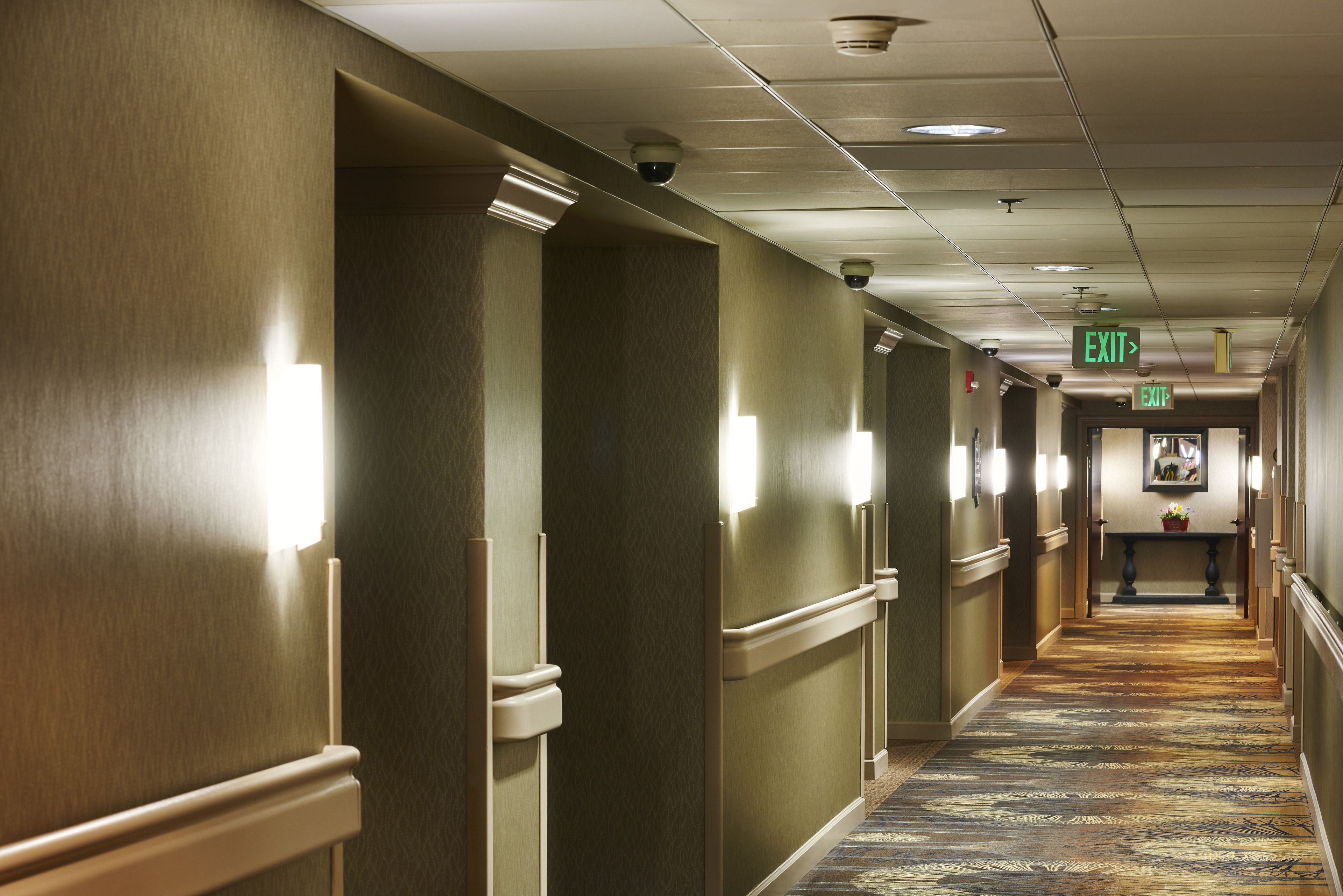 A hotel corridor with wooden paneling, exit signs, and a patterned carpet.