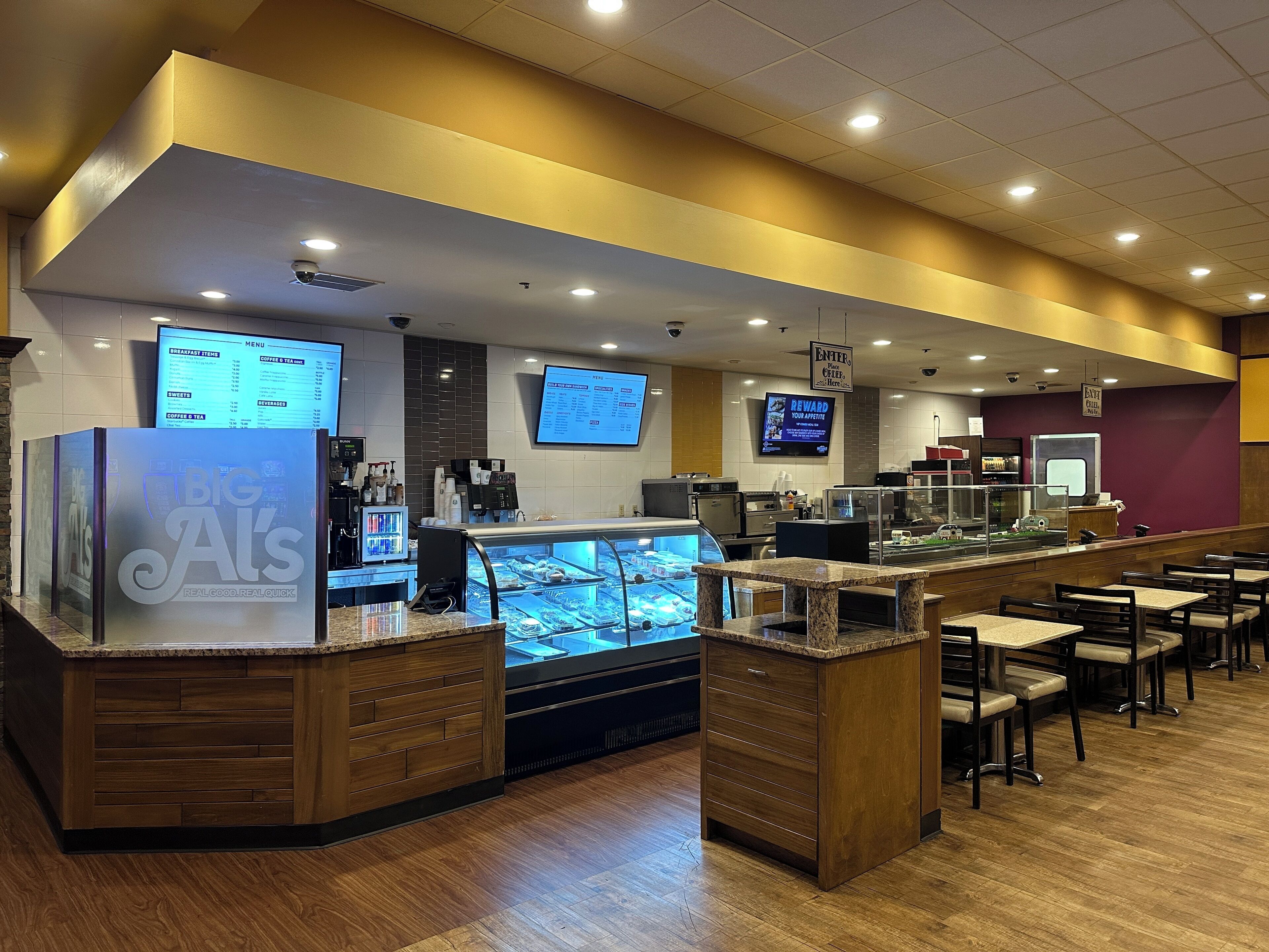 A modern coffee shop with a counter, digital menu boards, and seating area.
