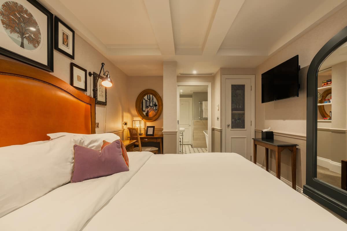 A hotel room with a bed, a desk, a chair, a television, and a bathroom visible through an open door.