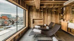 A wooden interior with a large window, two reclining chairs, a small table, and a shelf with towels. - King Street Townhouse (Manchester)