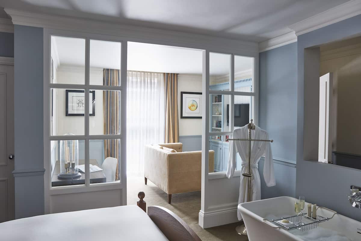 A hotel room with a large bed, a sitting area with a chair, a bathtub, and a bathroom with a mirror and sink.