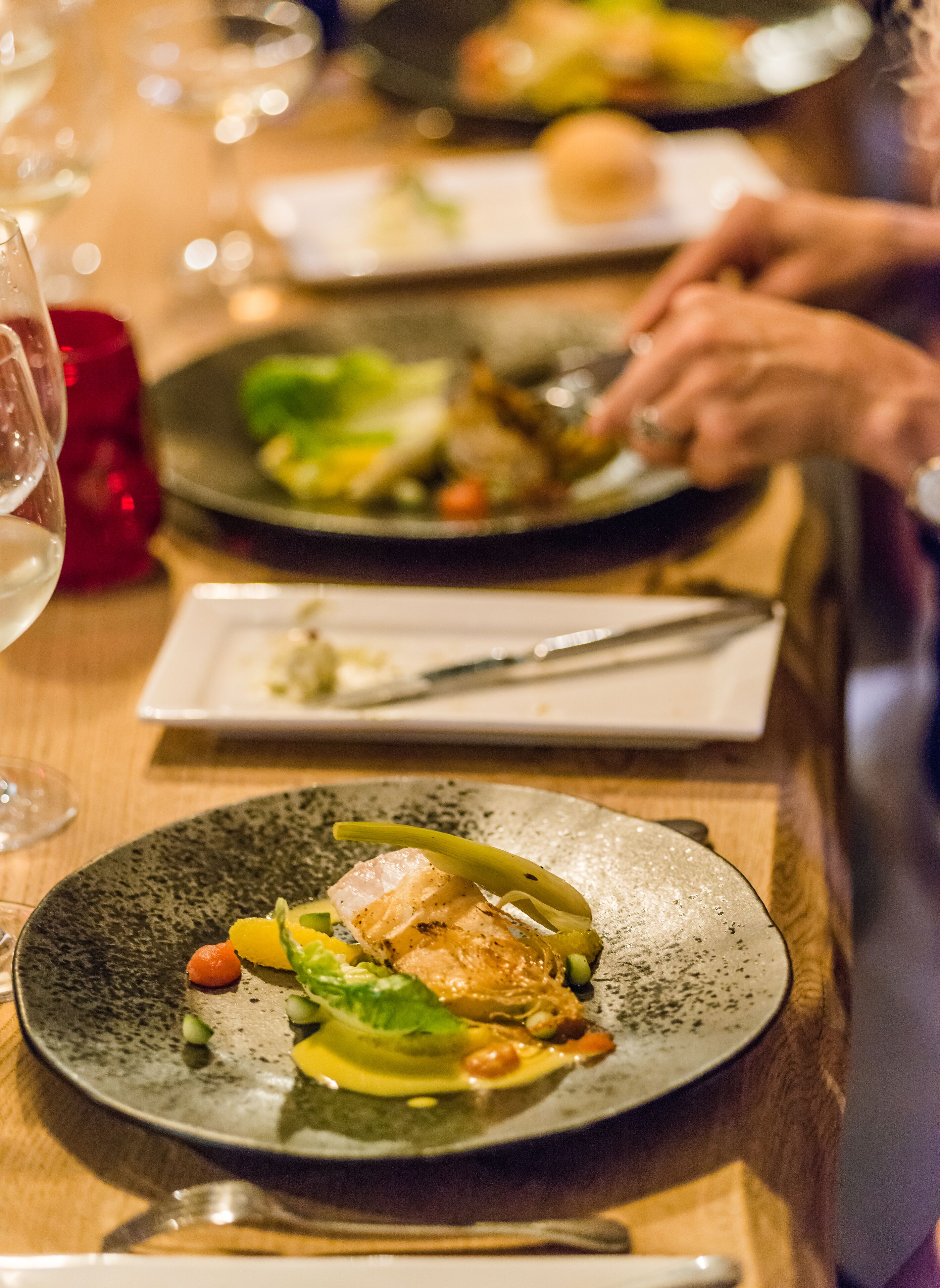 A dining table with plates of food, a wine glass, and cutlery.