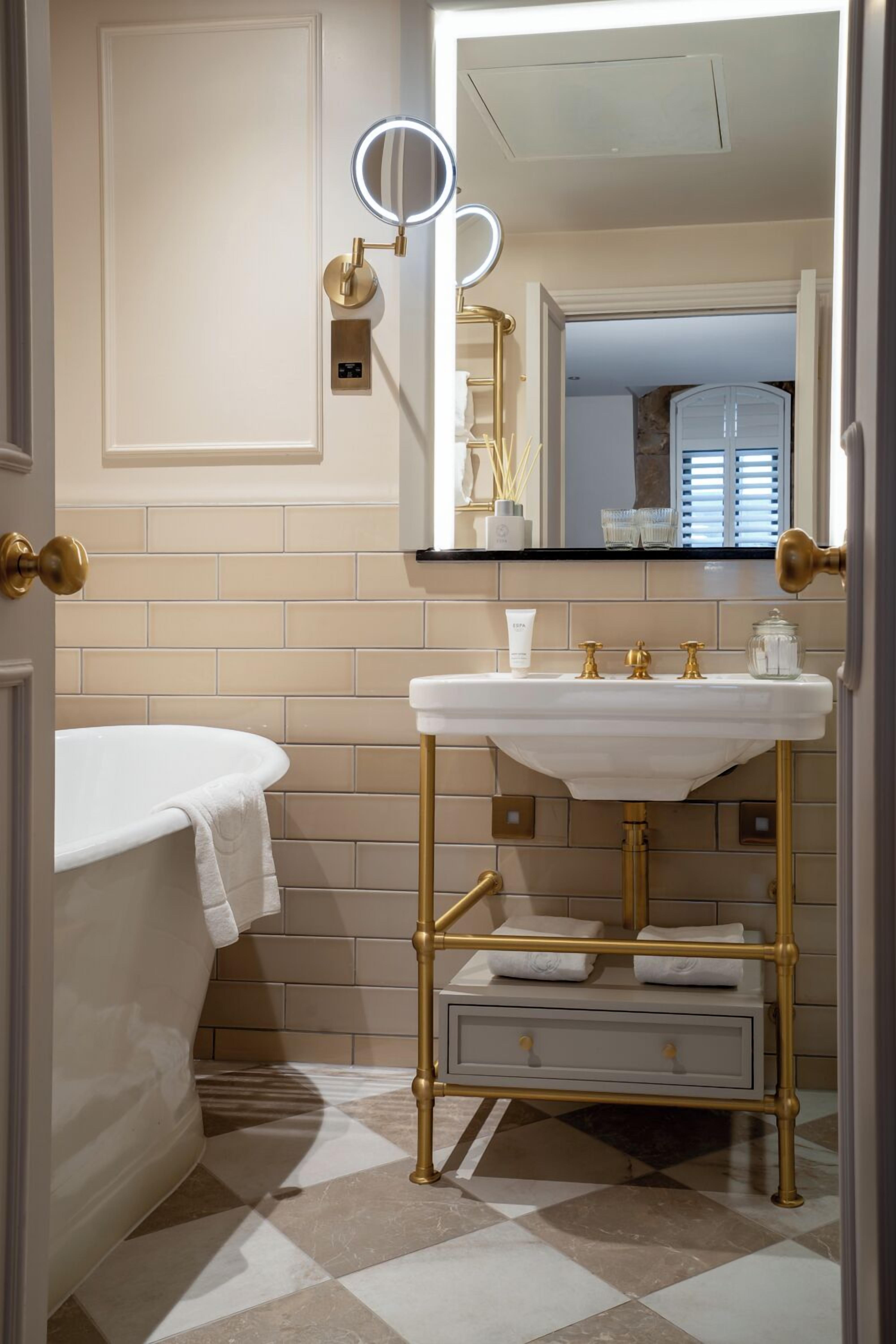 Un baño con un lavabo blanco, grifería dorada, un espejo con luz y suelo de cuadros.