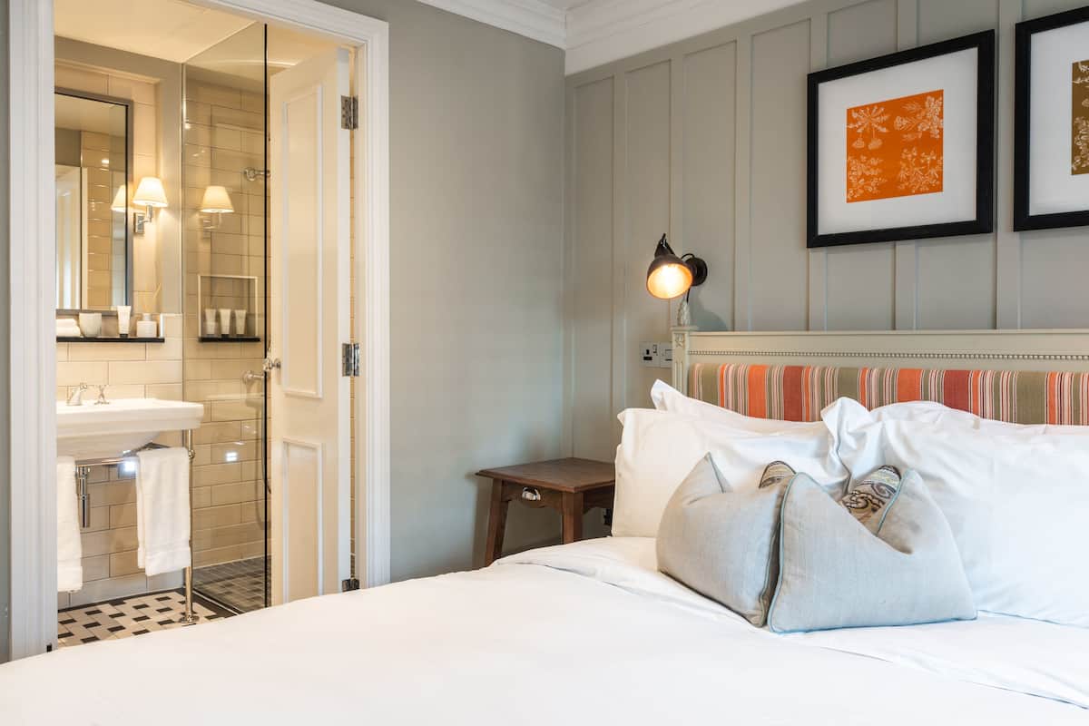 A hotel room with a bed, bedside table, lamp, and a bathroom with a sink and mirror.