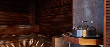 A sauna with wooden slats, a stone wall, and a metal heater.