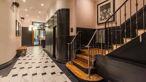 A hallway with a checkered floor, a staircase with black railings, and a framed artwork on the wall. - King Street Townhouse (Manchester)