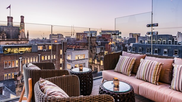 A high-rise room with wicker furniture, a glass table, and a city view. - King Street Townhouse (Manchester)